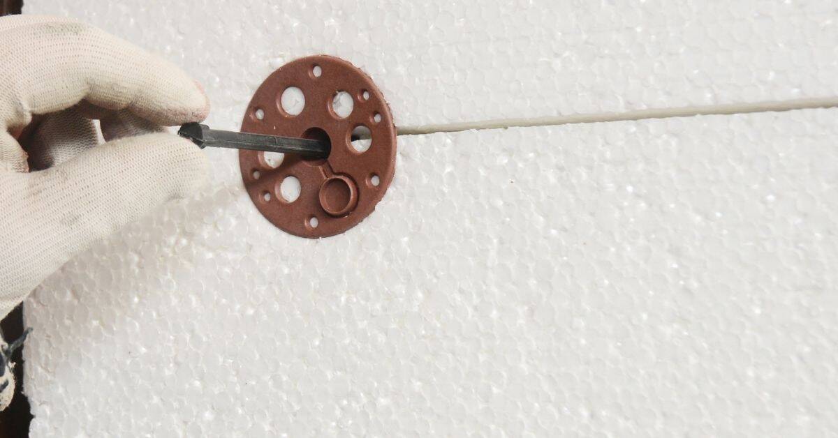 Hand wearing glove inserting anchor into foam board