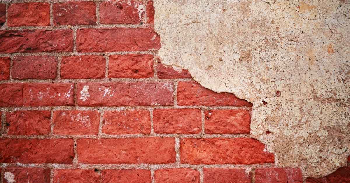 Red brick wall with peeling stucco render on right side