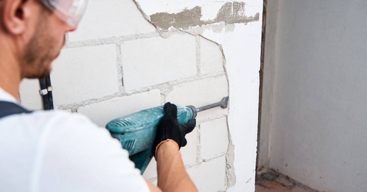 Person using power tool to remove stucco from block wall
