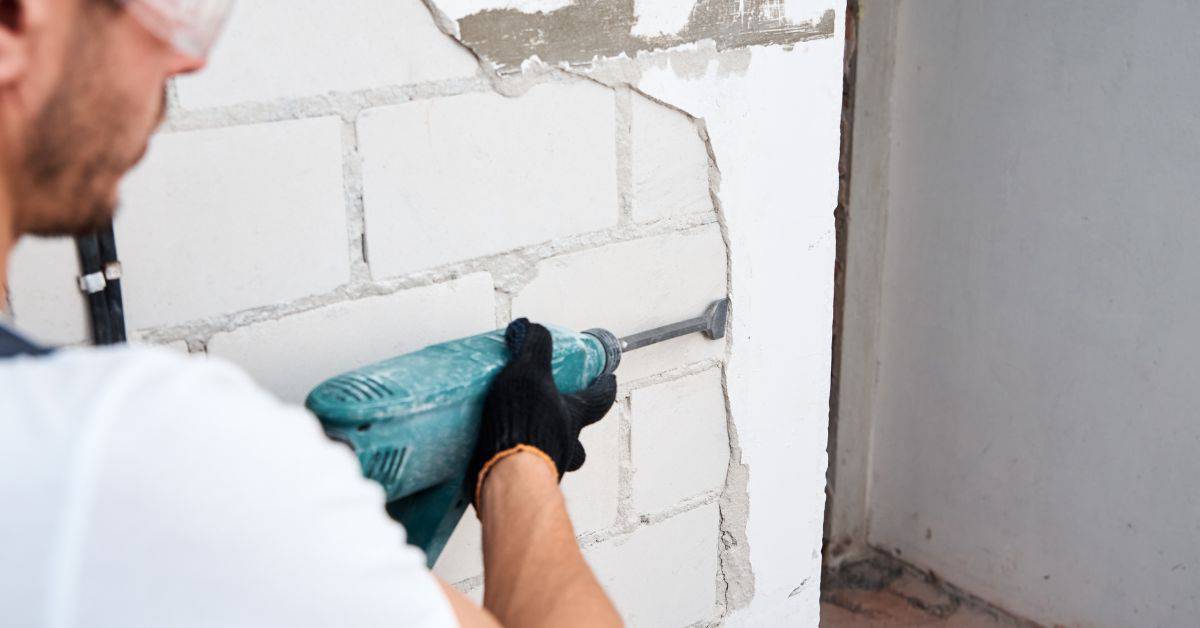 Person using power tool to remove stucco from wall
