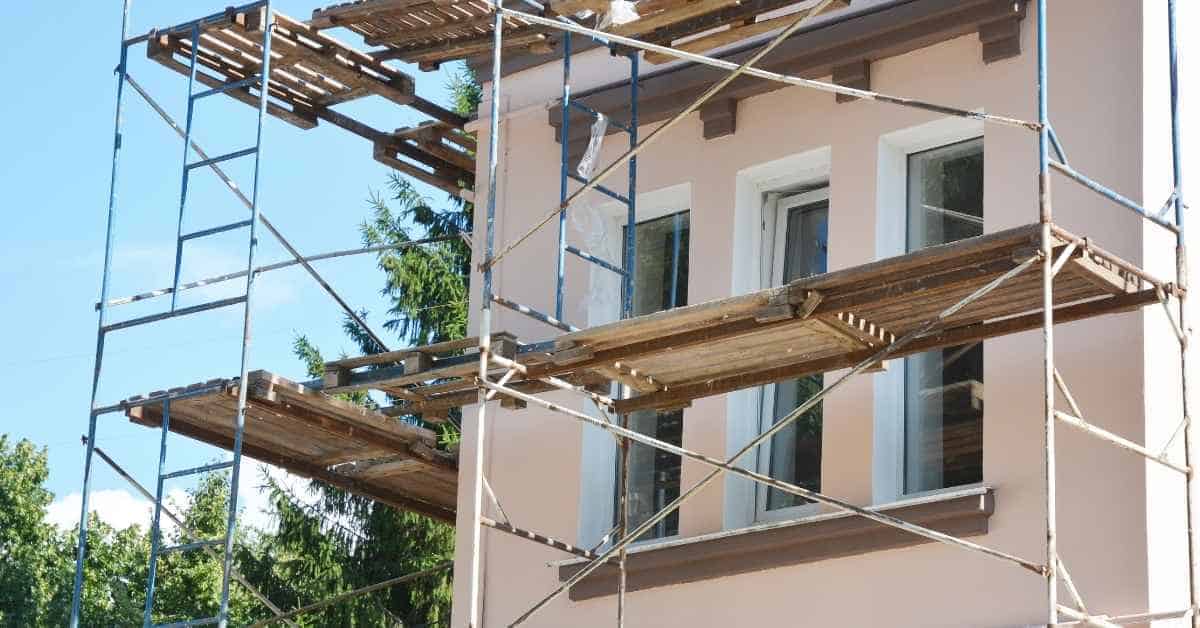 Scaffolding set up around exterior stucco wall with windows