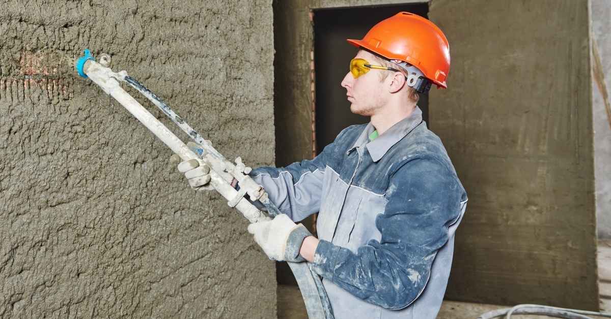 Worker spraying stucco scratch coat on wall