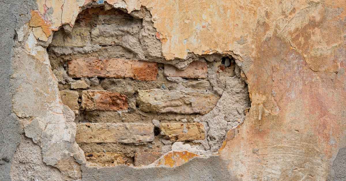 Damaged stucco wall with exposed brick underneath