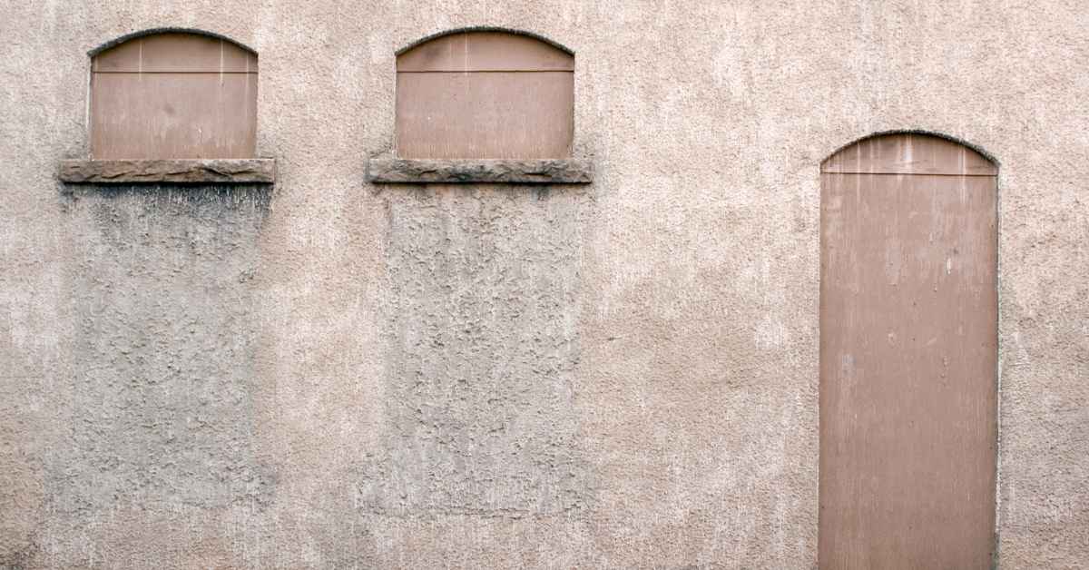 Stucco wall with closed window and door openings and visible discoloration stains
