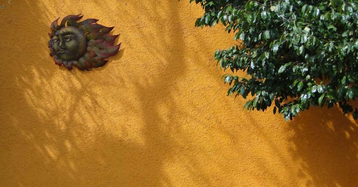 Textured yellow stucco wall with green leaves and sun decoration