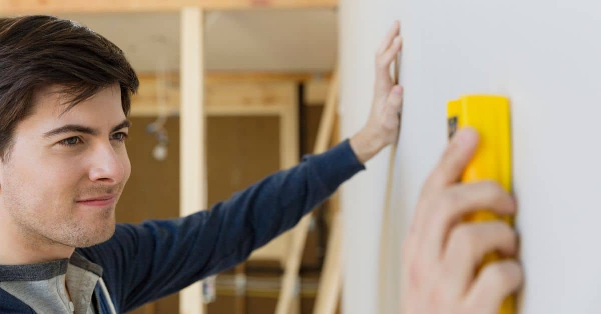 man using yellow stud finder on wall indoors
