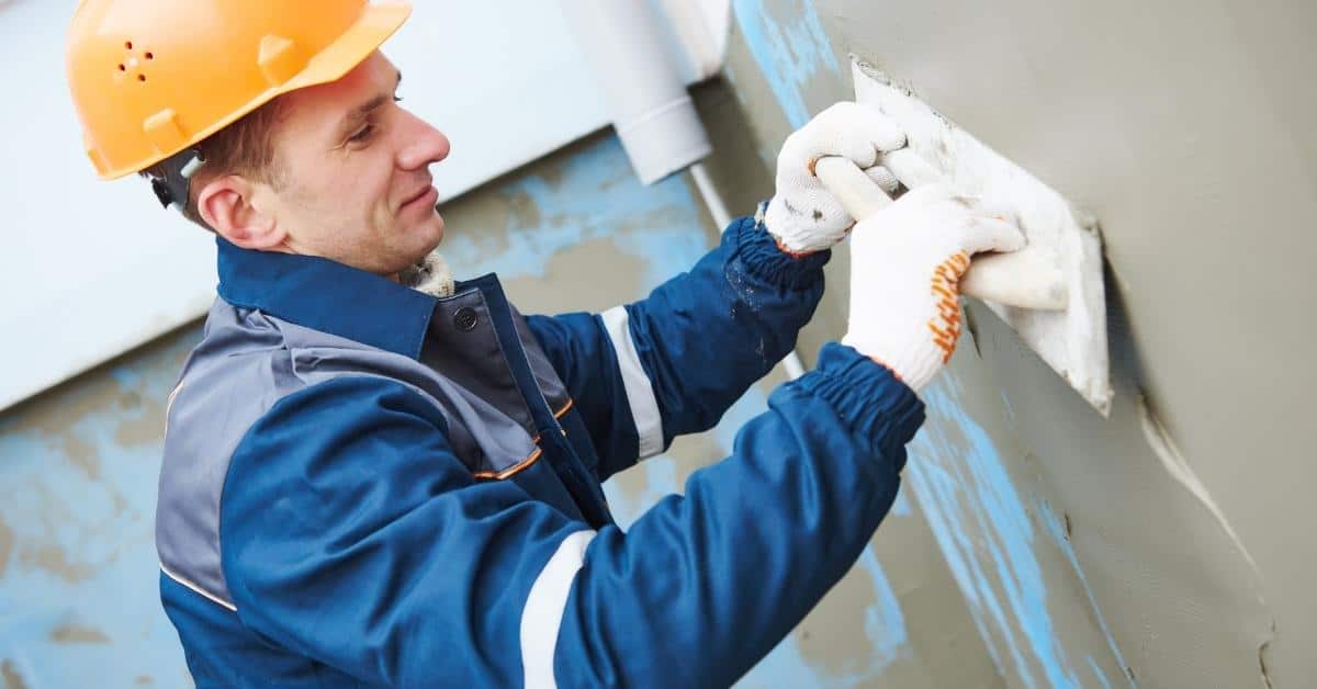 Worker wearing hard hat applying stucco with trowel