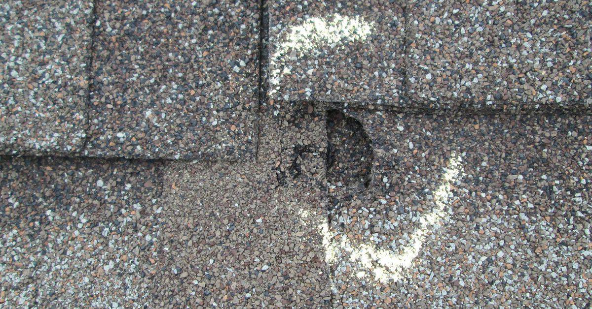 Damaged asphalt shingles with hole and white markings