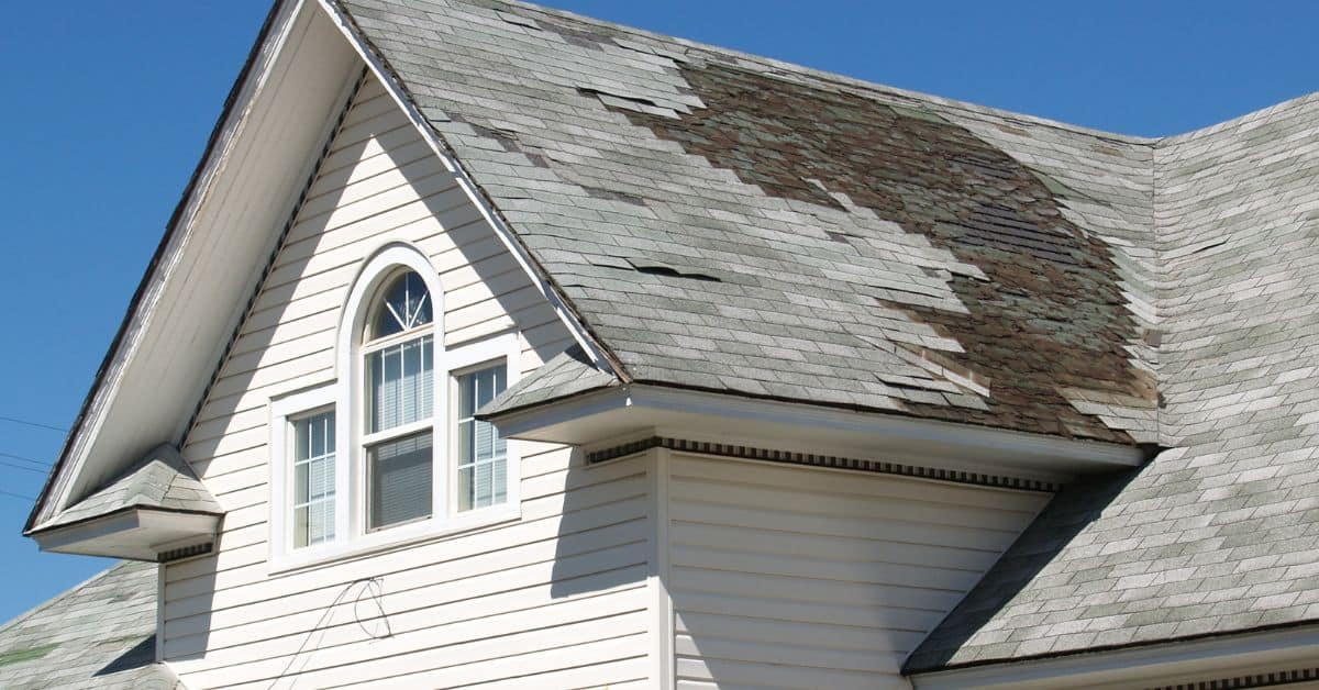 House roof with missing and damaged asphalt shingles