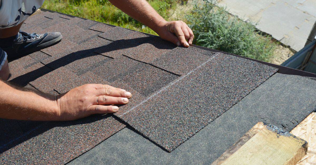 Person installing brown asphalt roof shingles on roof