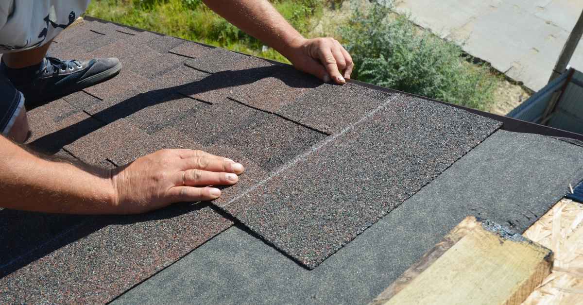 Hands installing asphalt shingles on a roof