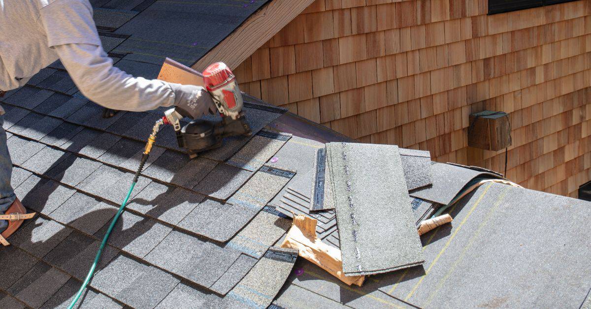 Person installing asphalt shingles on roof using nail gun