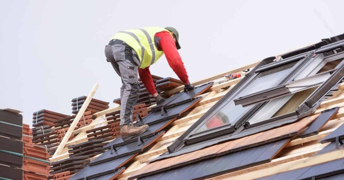 Worker installing dark roof tiles on sloped roof