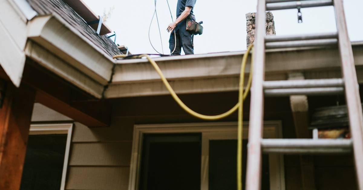 worker standing on roof edge with ladder and safety gear