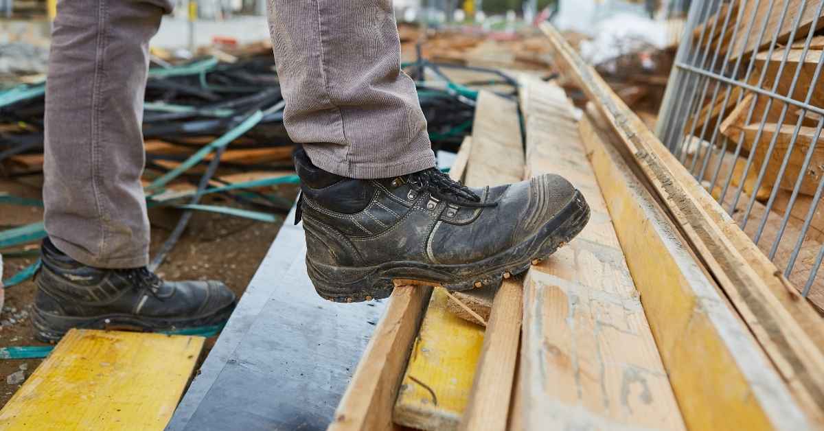 Person wearing black safety boots stepping on wooden planks
