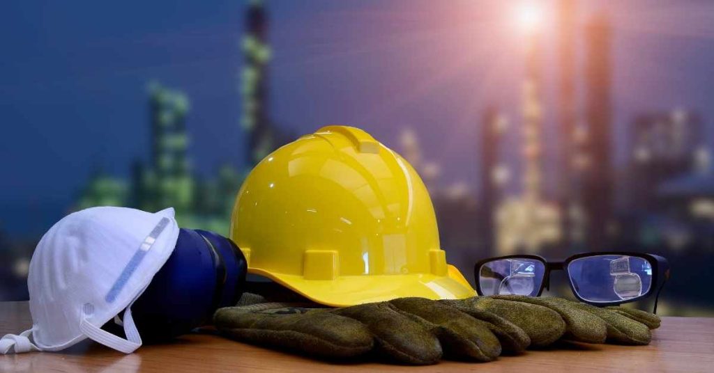 Yellow hard hat, safety gloves, white mask, and safety glasses on table