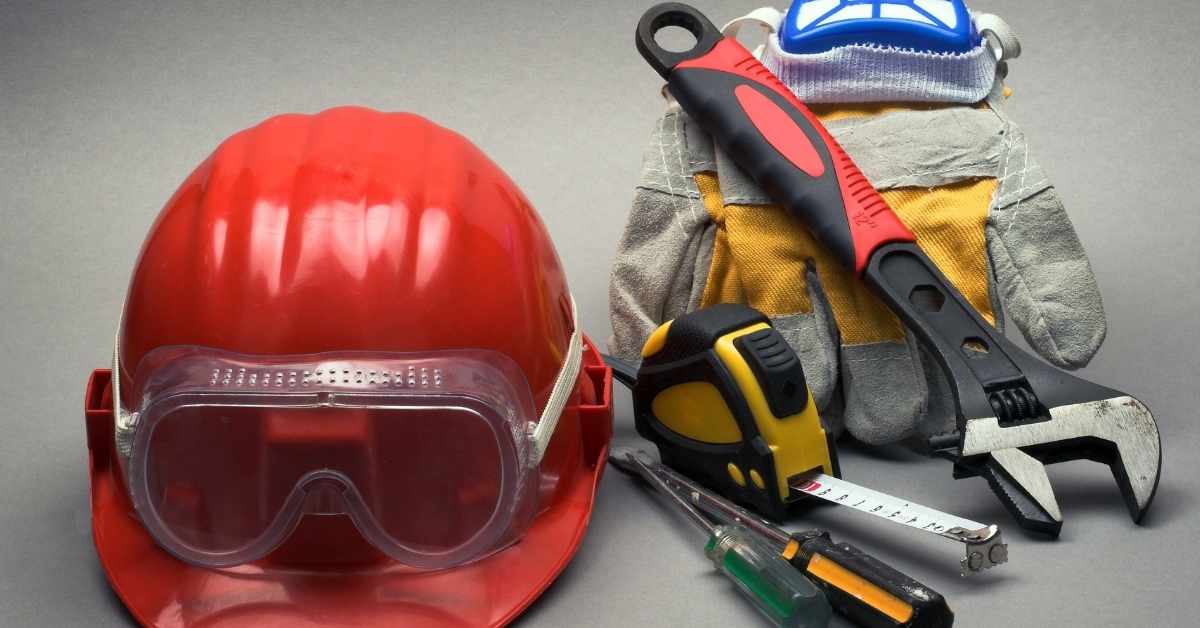 Red hard hat with goggles gloves tape measure wrench and screwdrivers