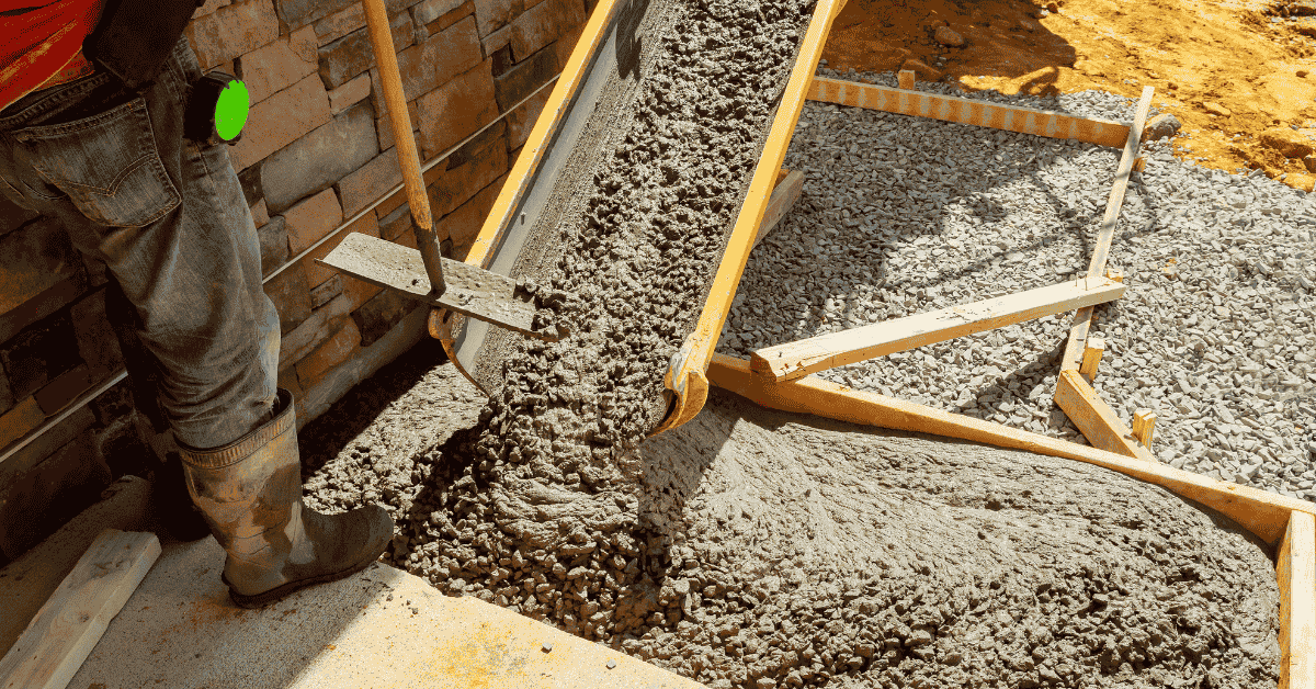 Worker pouring concrete from chute into wooden form on ground