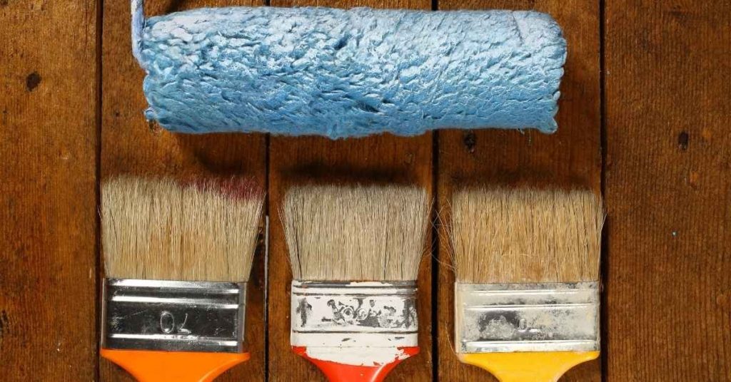 Three paintbrushes and one paint roller on wooden surface