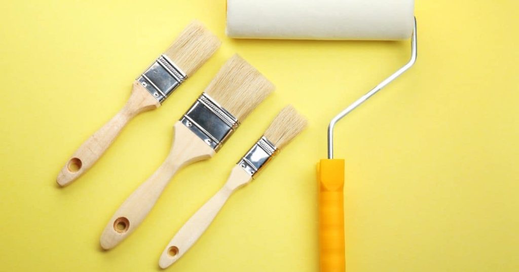 Three paintbrushes and one paint roller on yellow background