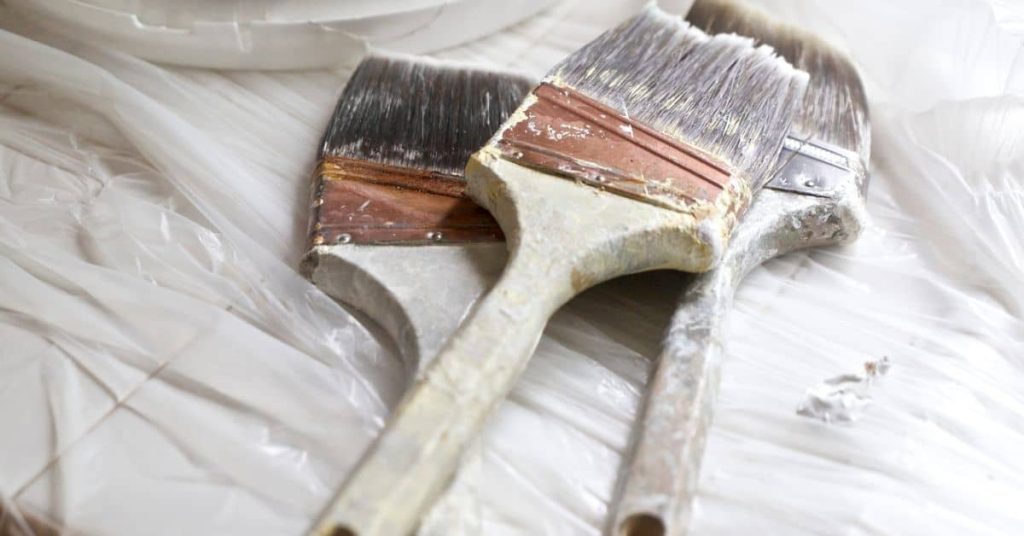 Three paintbrushes with dried paint on plastic sheet