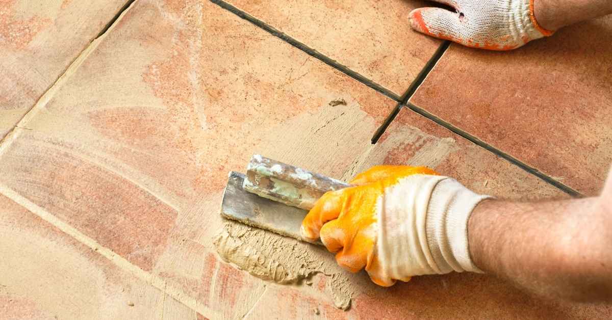 Hands applying grout between ceramic floor tiles