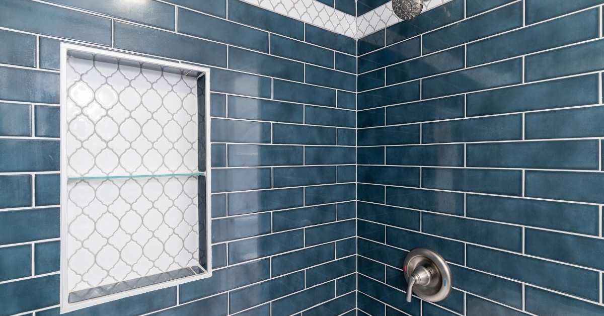 Blue subway tiles surrounding white patterned shower niche with glass shelf