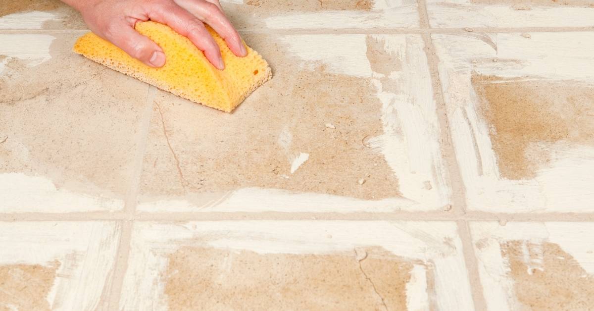 Hand holding yellow sponge cleaning tile grout