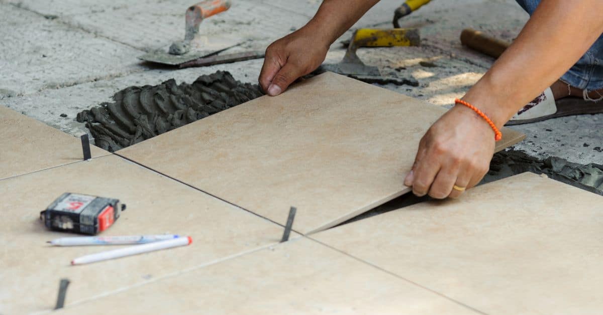 Hands placing a tile on floor with tools nearby