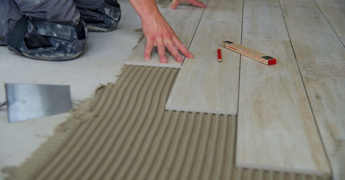 Person installing wood-look floor tiles on adhesive mortar