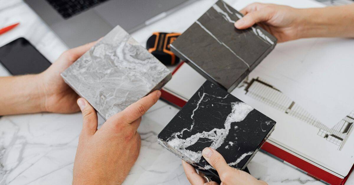 Hands holding three marble-patterned tile samples on table
