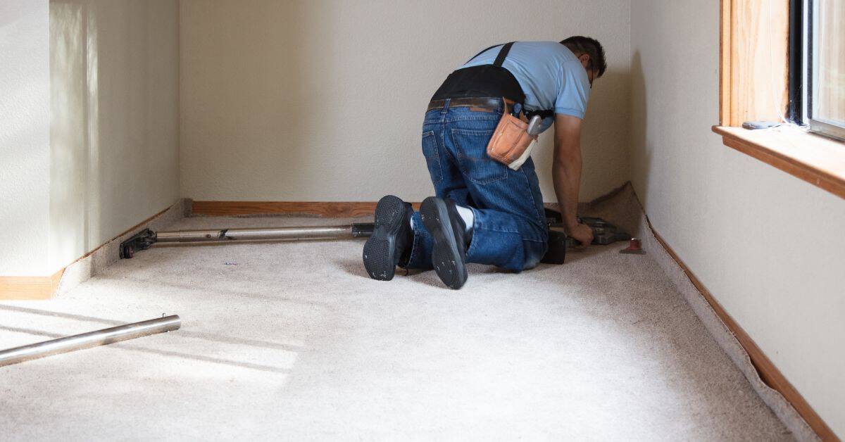 Person kneeling on carpeted floor with tools nearby