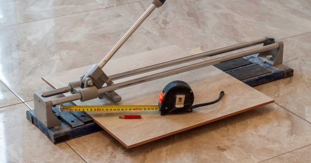 Tile cutter with tape measure and pencil on tiled floor