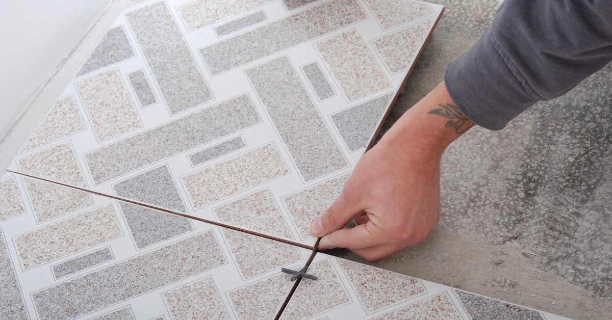 Hand placing tile spacer between two floor tiles