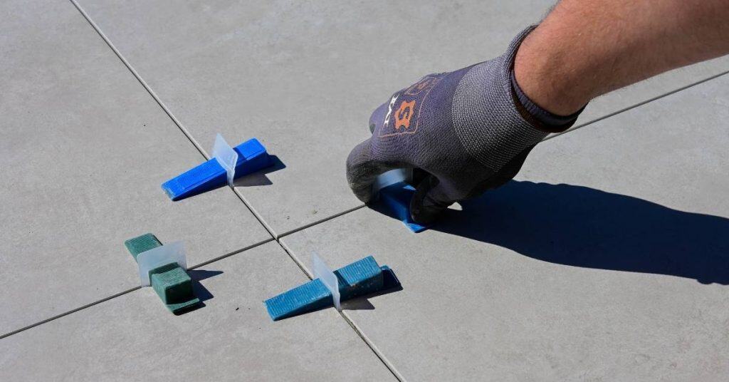 Hand placing blue tile leveling wedge on gray floor tiles