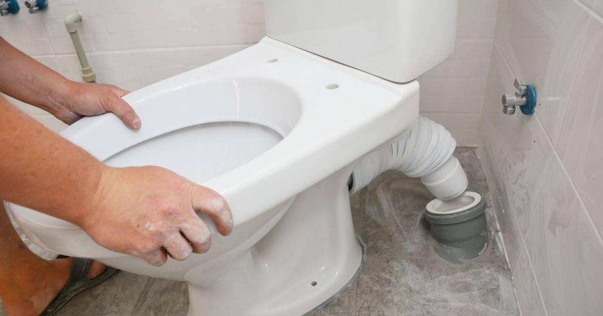 Person installing white toilet bowl on bathroom floor