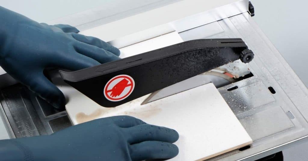 Hands in gloves cutting tile on a wet tile saw