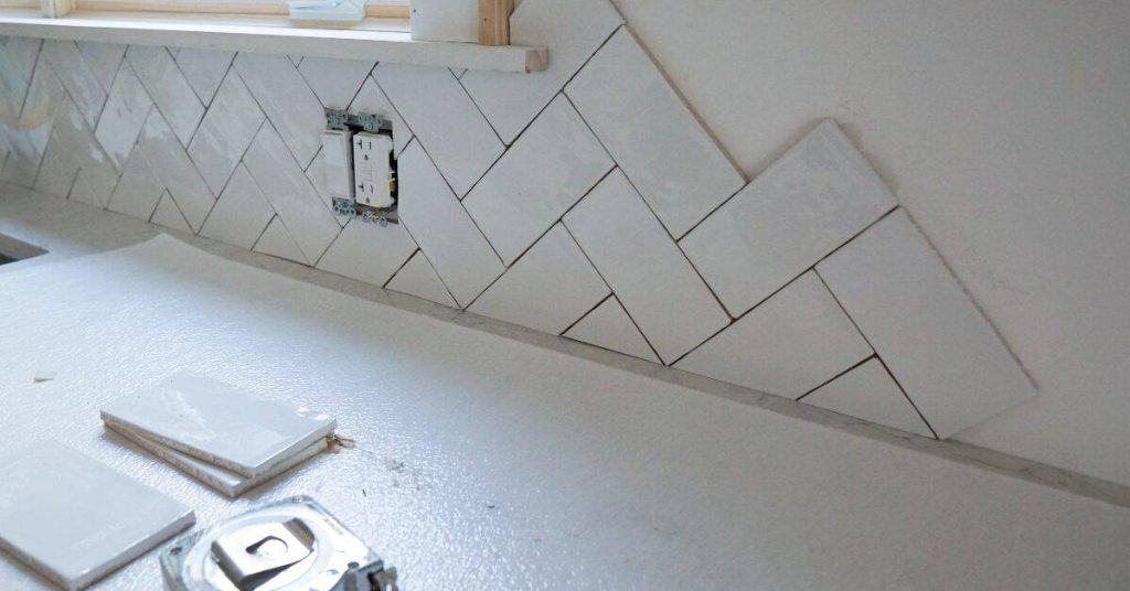 white herringbone tile backsplash partially installed without grout