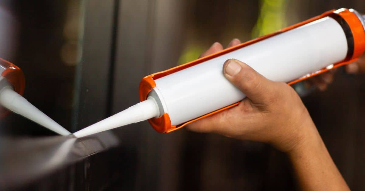Hand holding caulking gun applying white caulk to surface