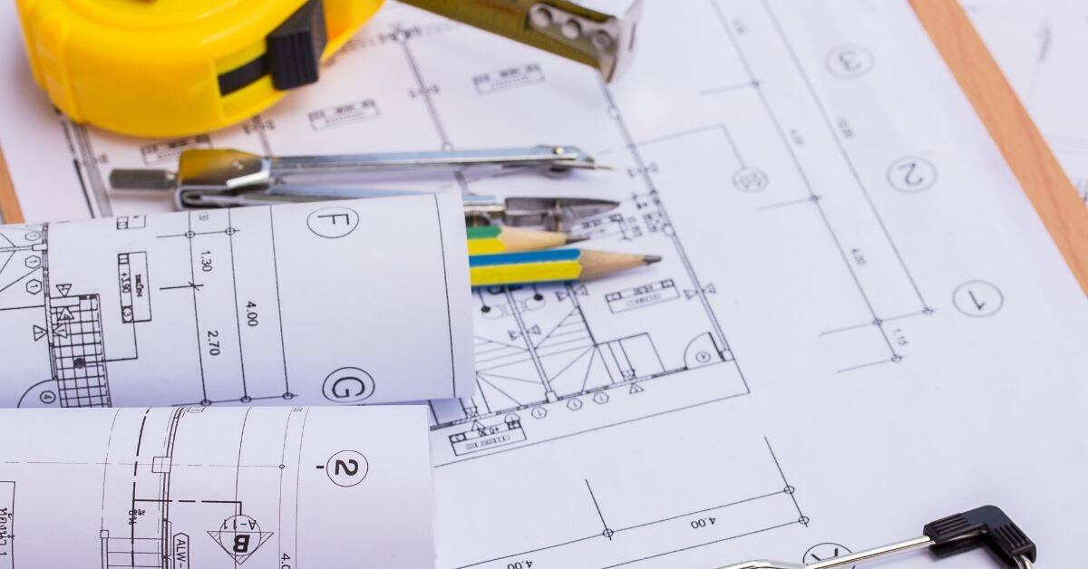 Tape measure pencils compass and rolled blueprints on table