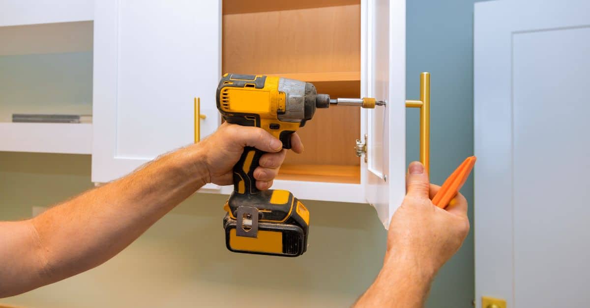 Person using cordless drill on cabinet door handle