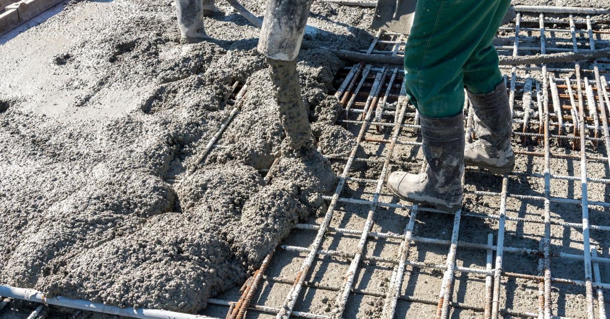 Wet concrete being poured over steel rebar with worker standing