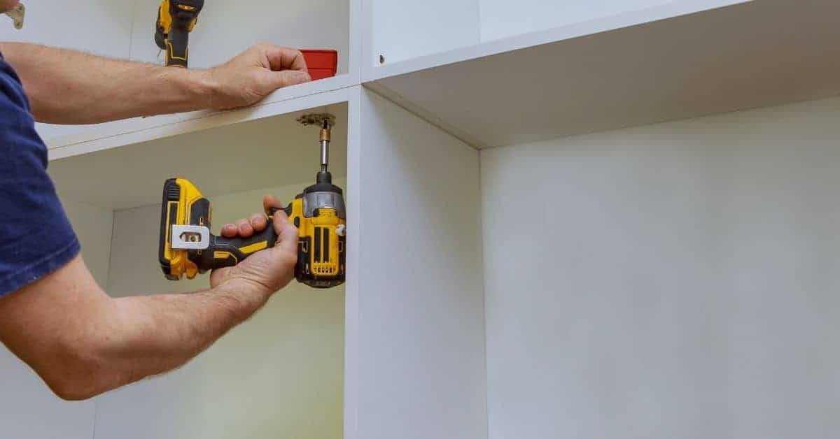 Person using cordless drill to remove screws from white cabinet