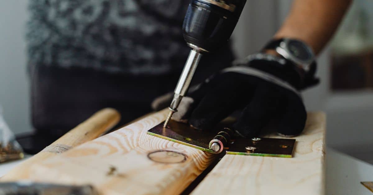 person using power drill to screw metal bracket onto wood