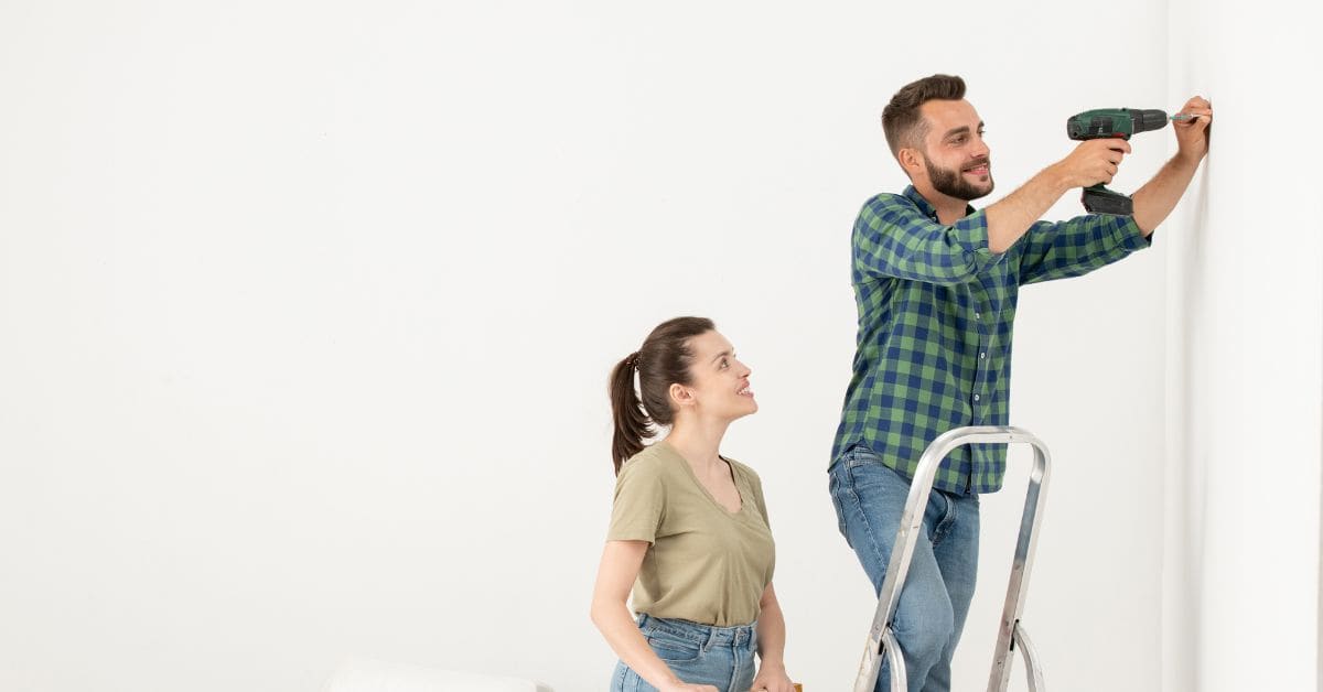 Man using cordless drill on wall with woman watching