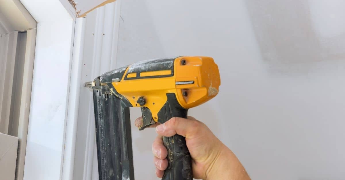 Hand holding yellow and black nail gun near white door frame