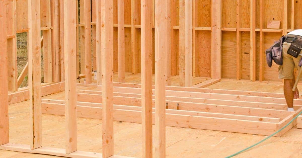 Wooden wall studs framing under construction with worker measuring