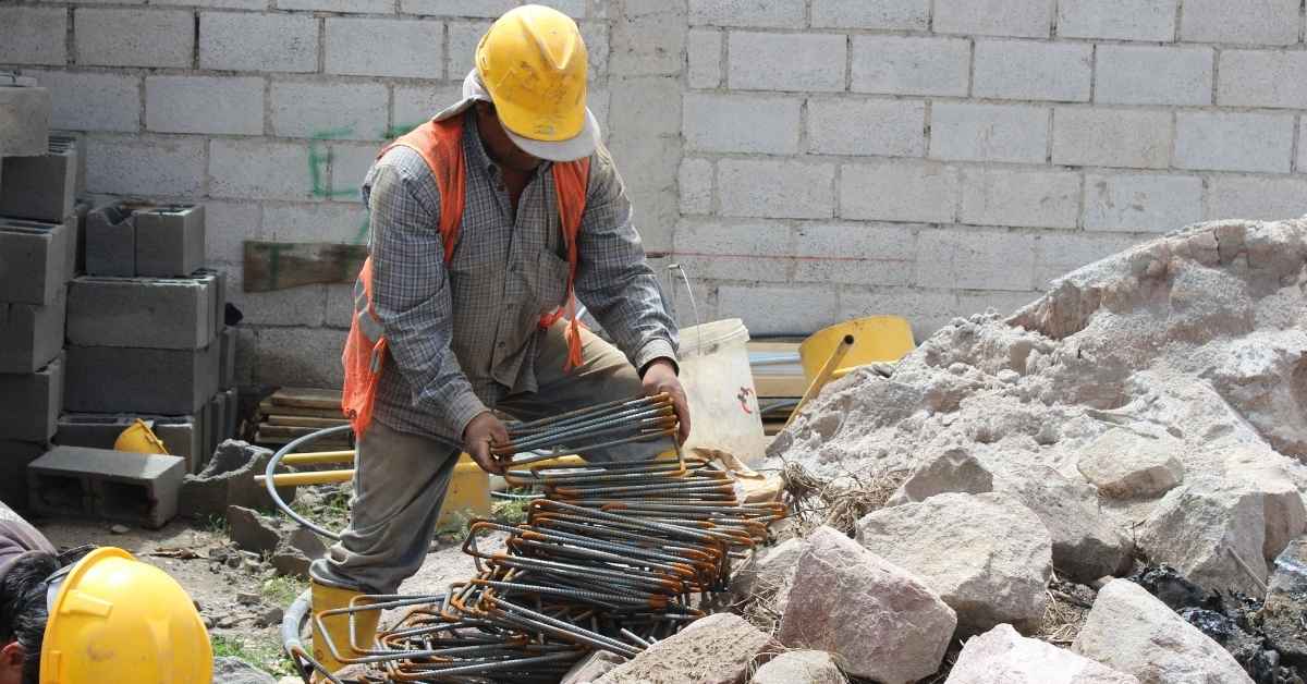 Construction worker handling rusty rebar at building site