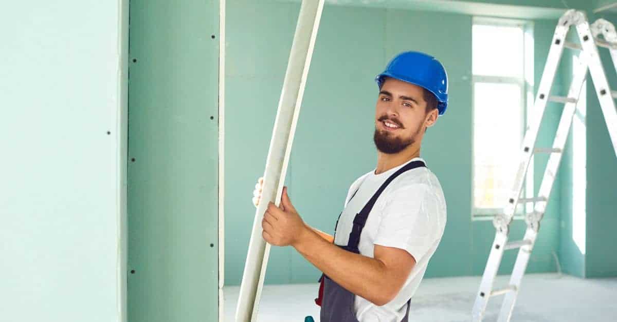 Worker holding a drywall panel inside a room under construction