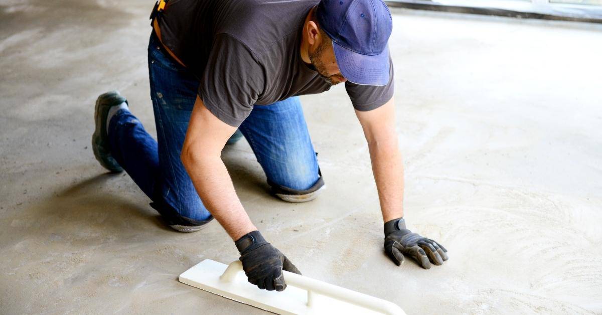 Worker kneeling and smoothing wet concrete slab with float tool